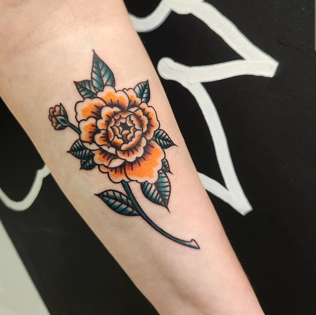 An orange rose tattoo with green leaves on a person's forearm.