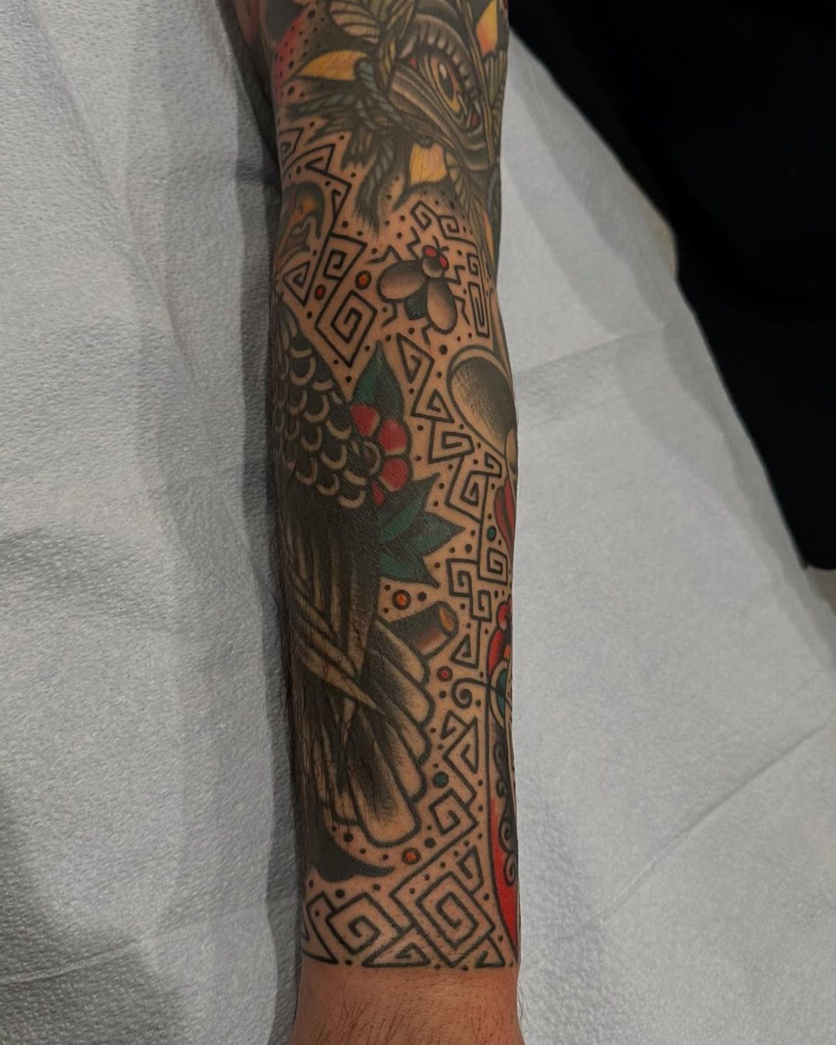 A person's arm covered in American traditional tattoos with intricate geometric pattern filler.