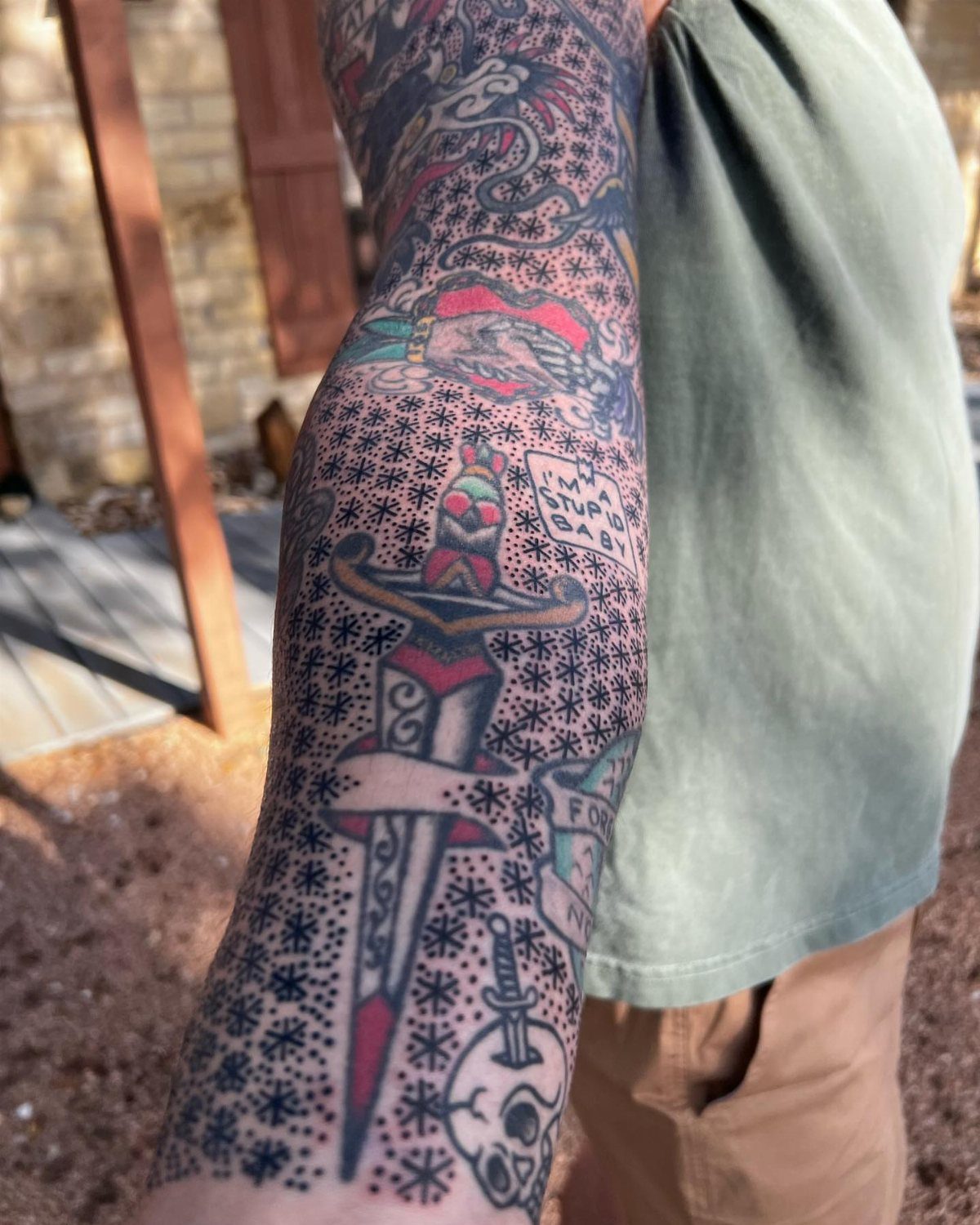 A person's arm featuring traditional tattoos surrounded by small black ink stars and dots.