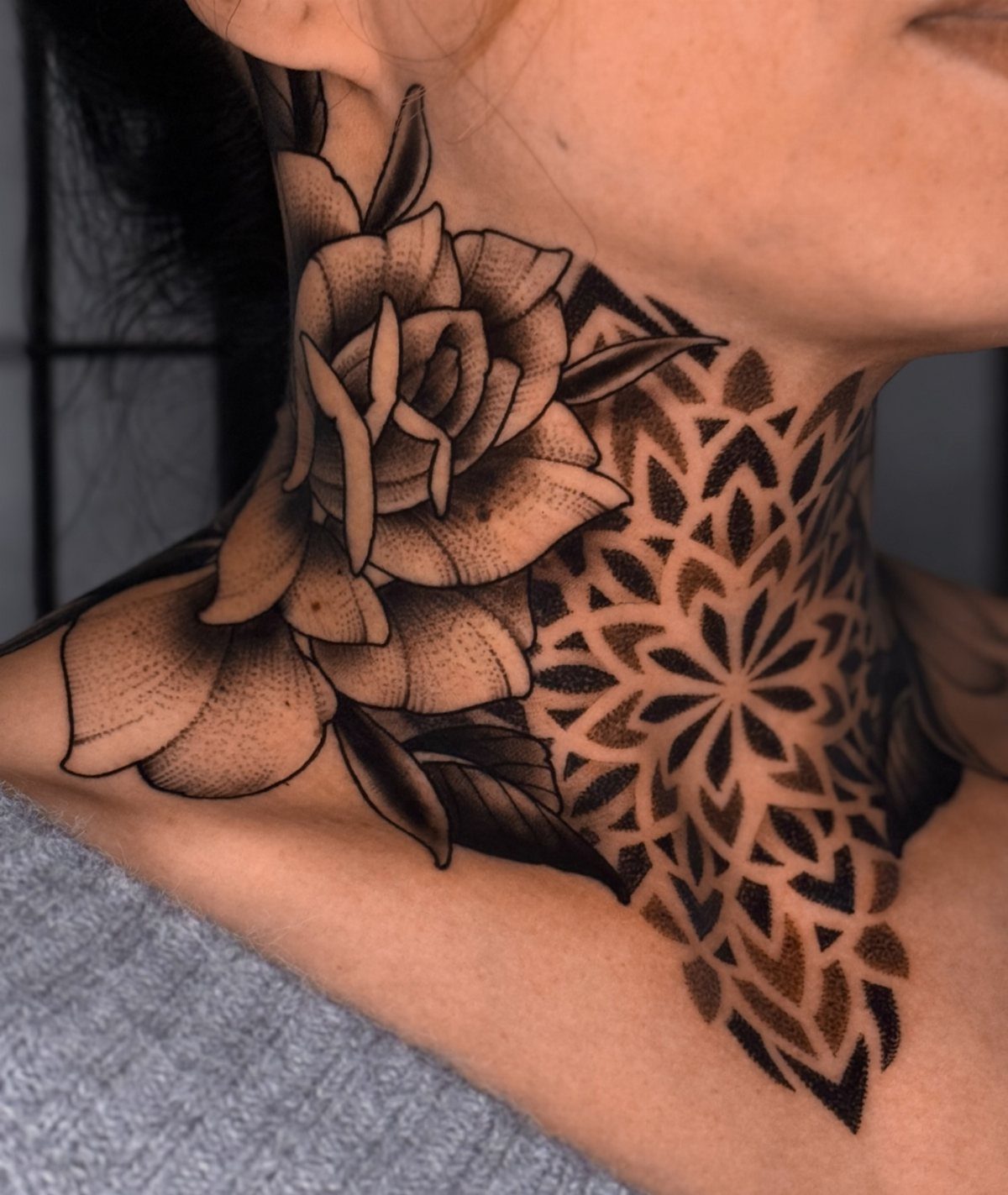 A large black ink rose and geometric mandala tattoo on a person's neck.