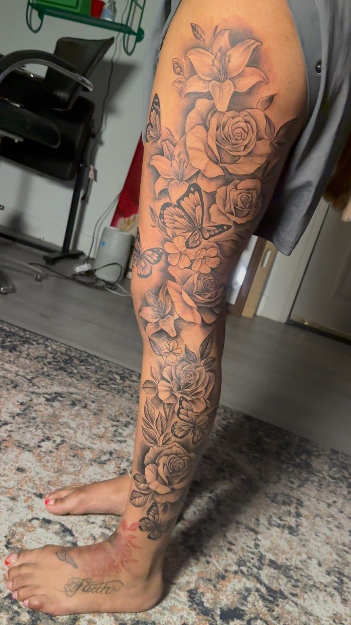 Large black and grey floral tattoo with roses and butterflies covering a person's entire leg.