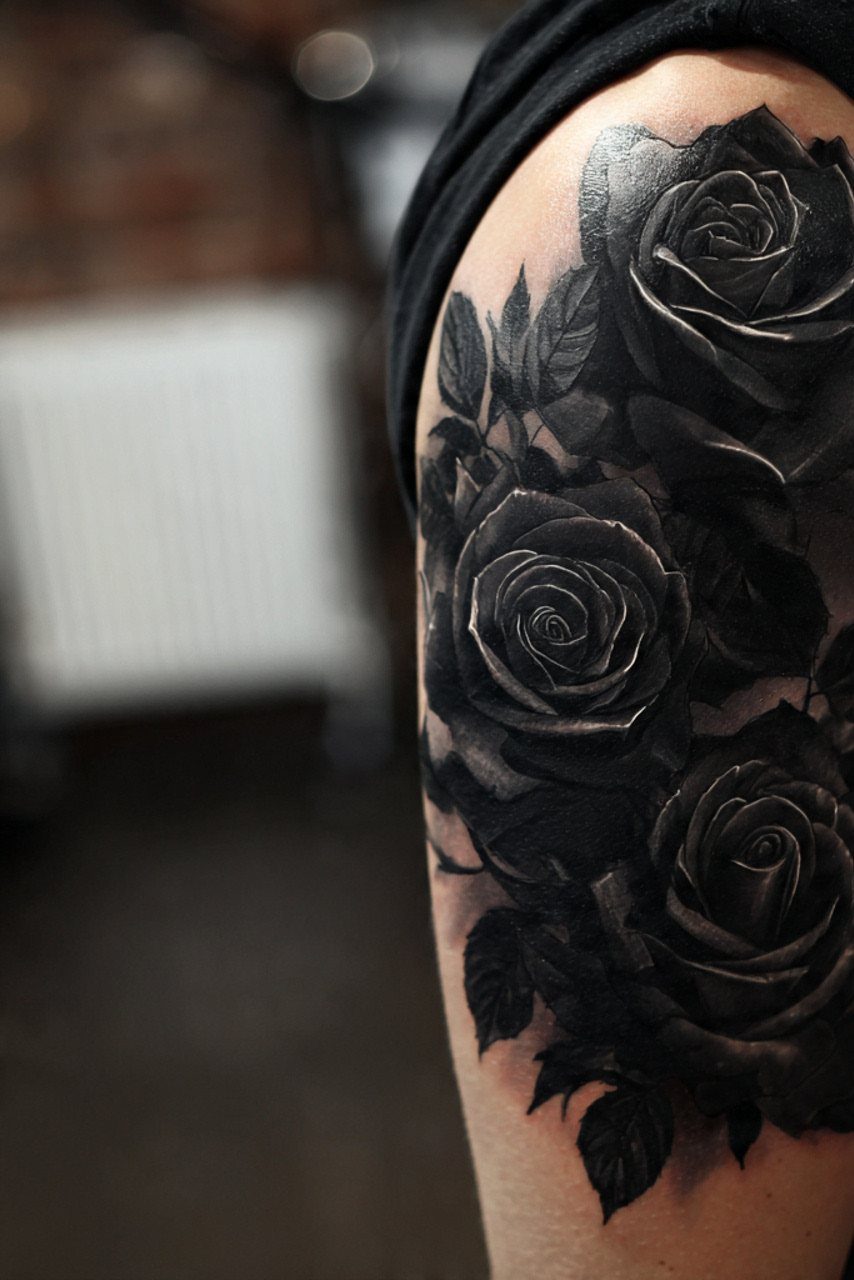 Large black and grey rose tattoos with detailed petals and leaves on a person's arm.