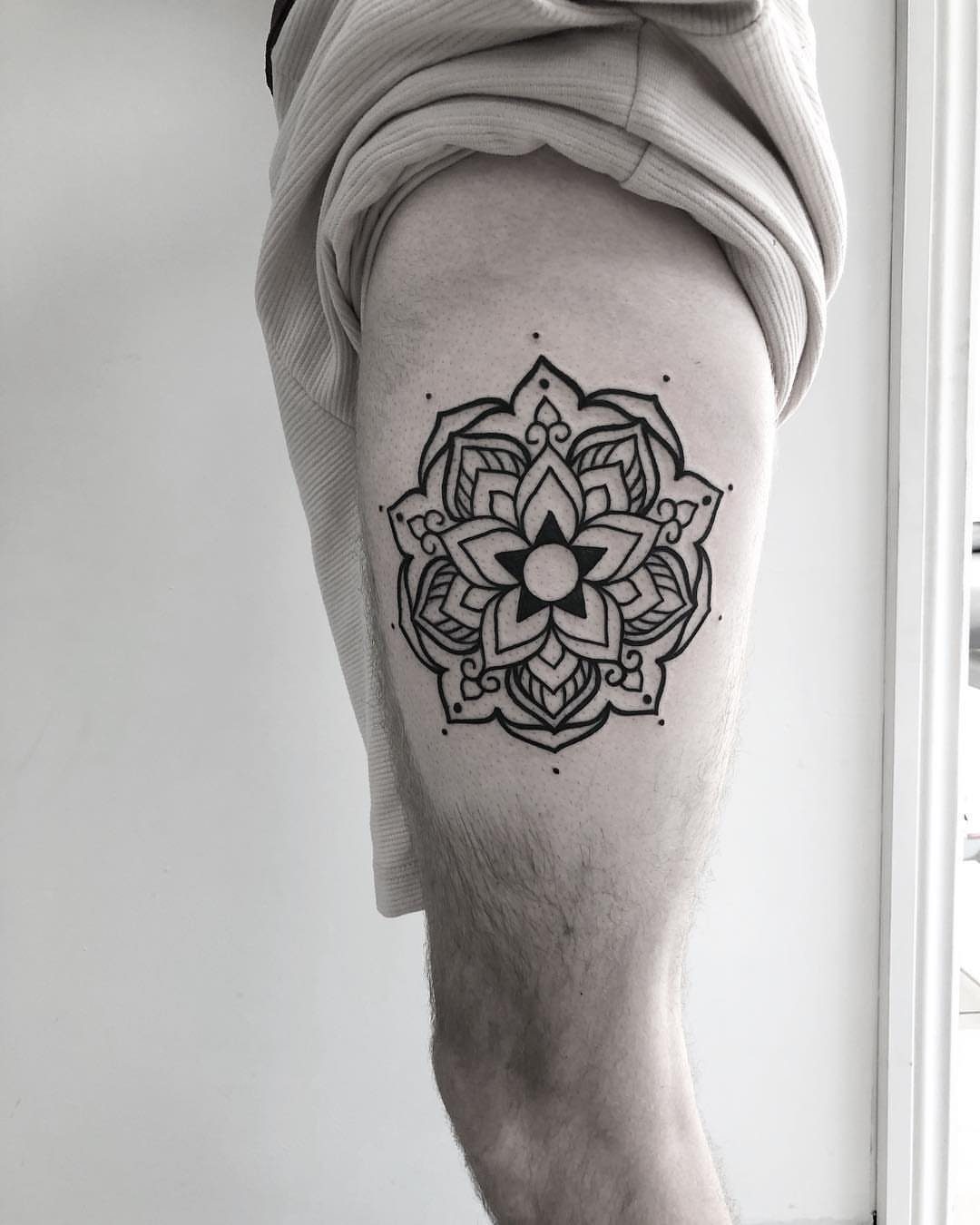 A black ink mandala flower tattoo with thick outlines on a person's thigh.