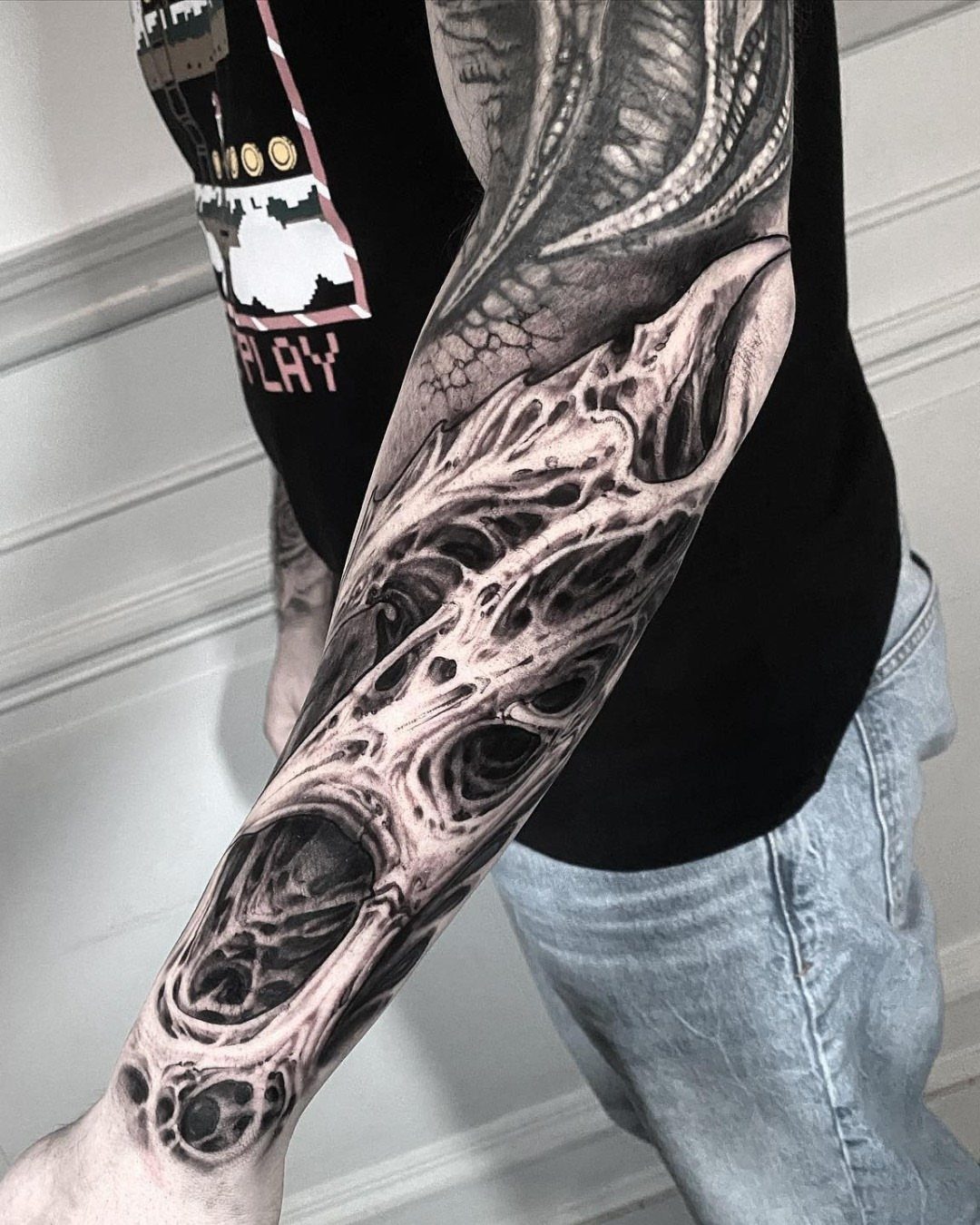 A detailed blackwork tattoo with organic, biomechanical textures covering a person's entire arm.
