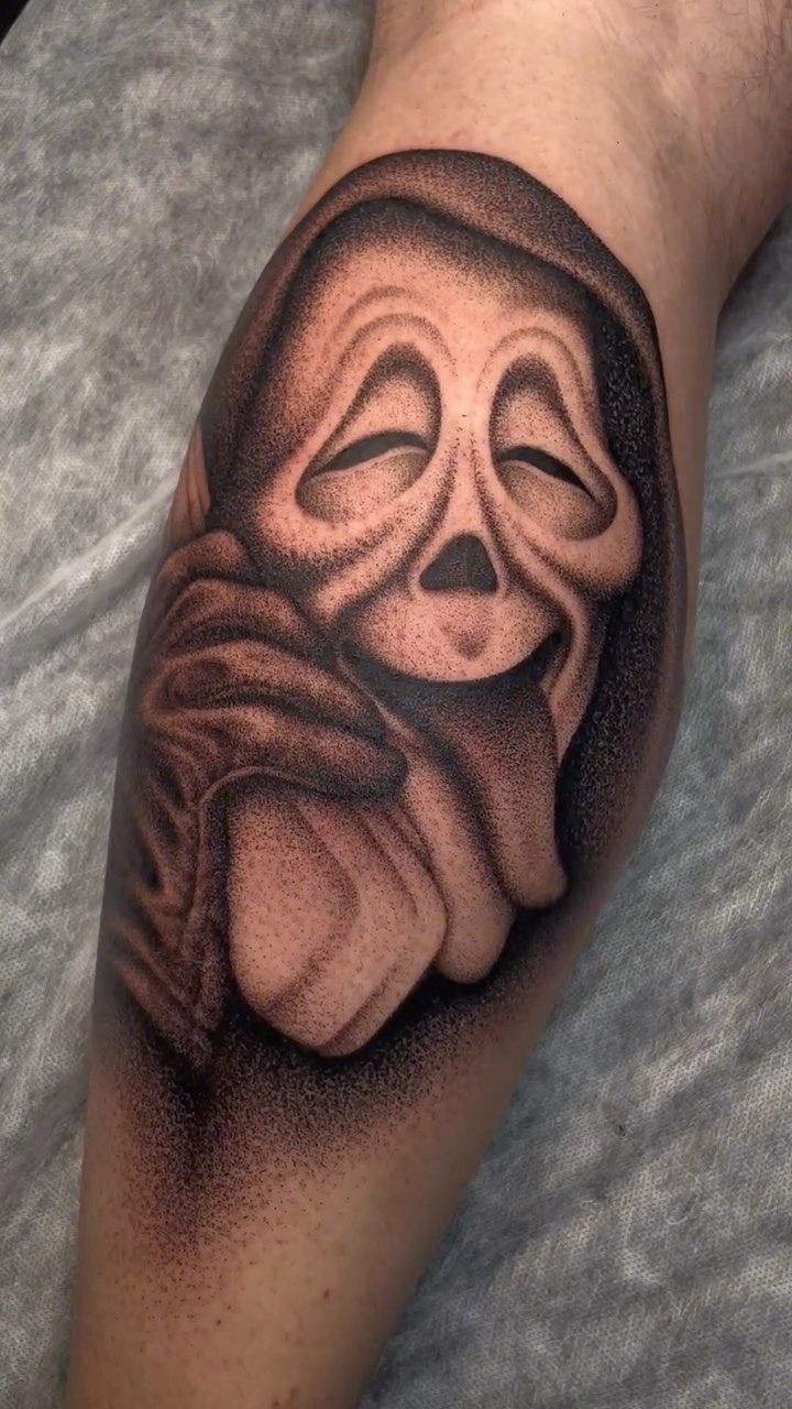 A black and grey ghost mask tattoo with heavy dotwork shading on a person's leg.