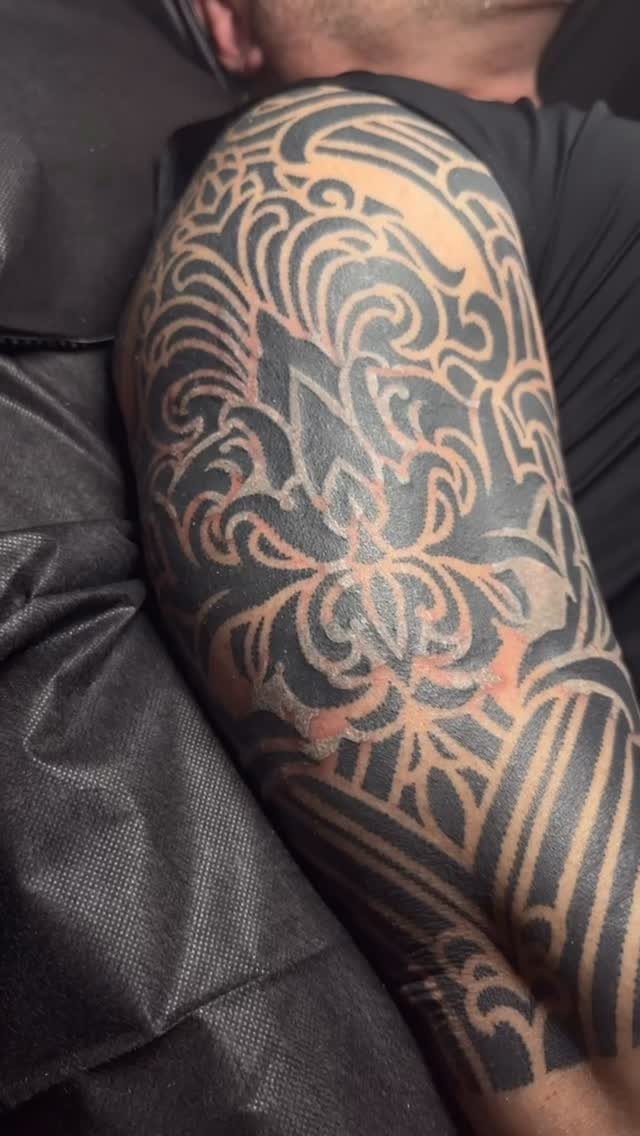 Intricate blackwork tattoo with swirling patterns and negative space on a person's arm.