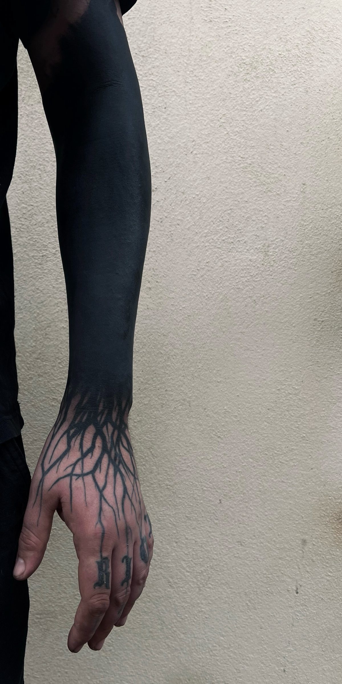 A person's arm with a solid black forearm tattoo and intricate linework on the hand.