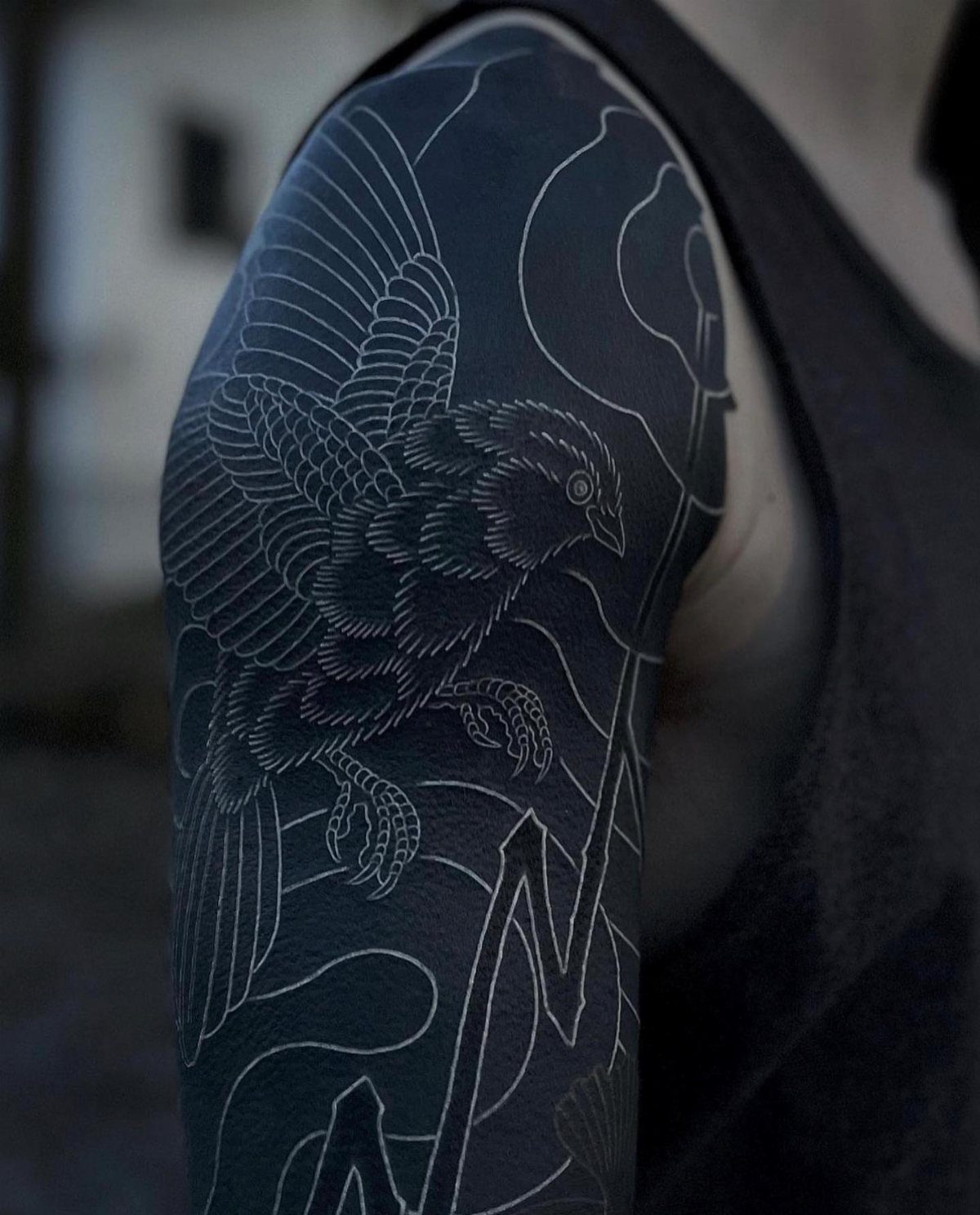 A large blackwork tattoo of a bird with intricate white linework on a person's arm.