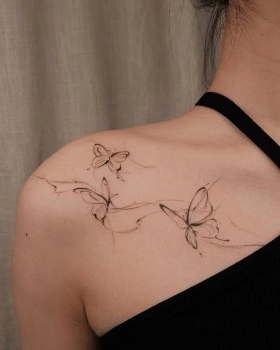 Three delicate black ink butterfly tattoos flowing across a person's shoulder and collarbone.