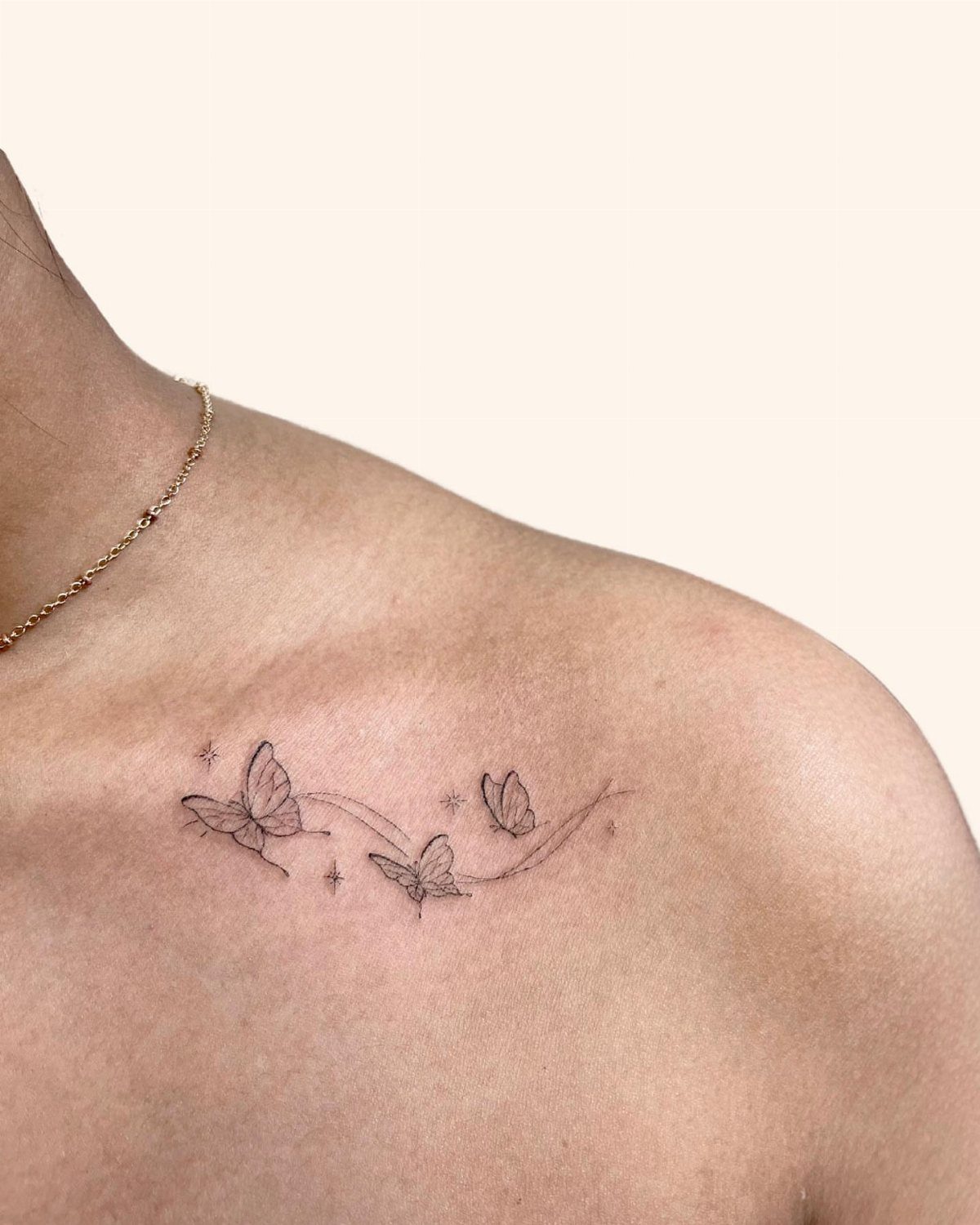Three small black ink butterfly tattoos following the natural curve of a person's collarbone.