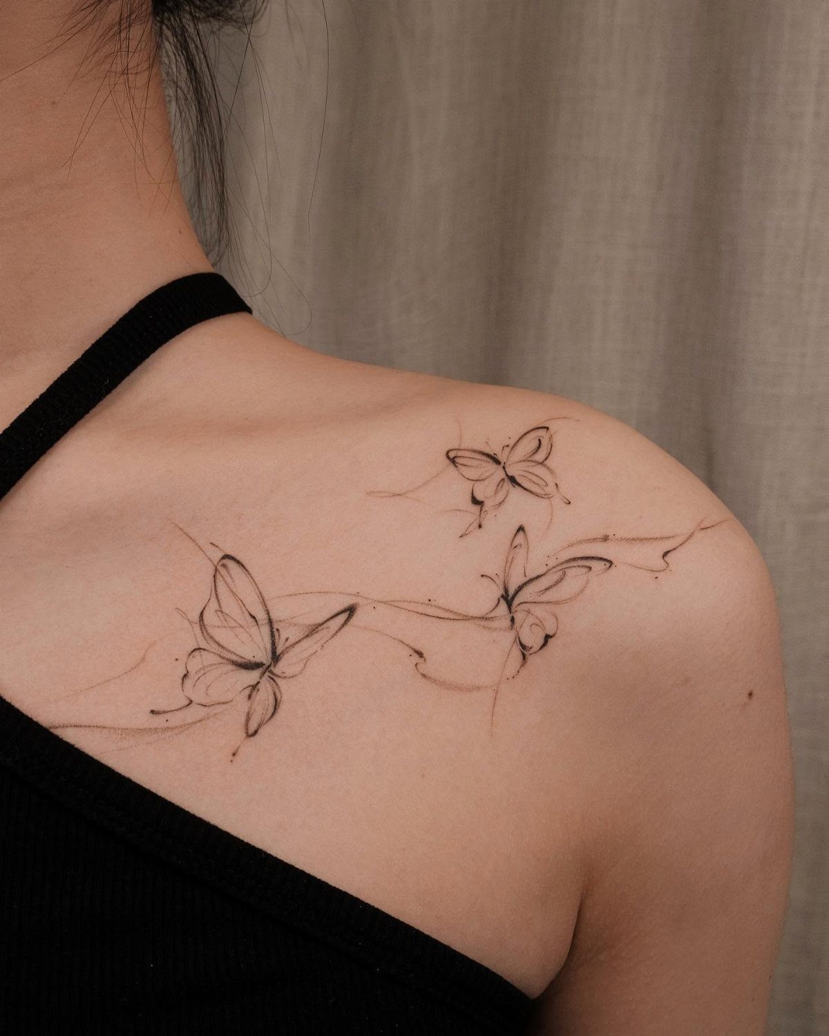 Three delicate black ink butterfly tattoos fluttering along a person's collarbone and shoulder.