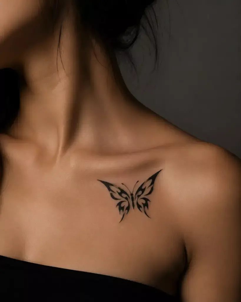Black ink butterfly tattoo with open wings on a person's collarbone.