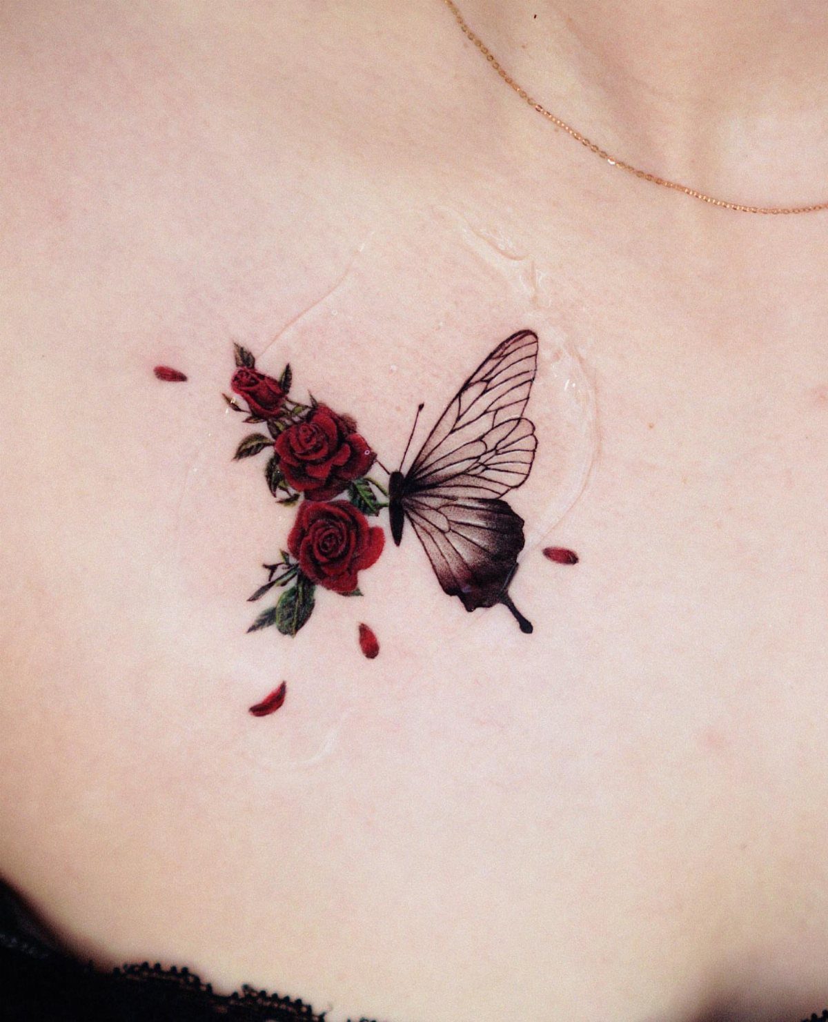 Butterfly tattoo with red roses and green leaves on a person's skin.