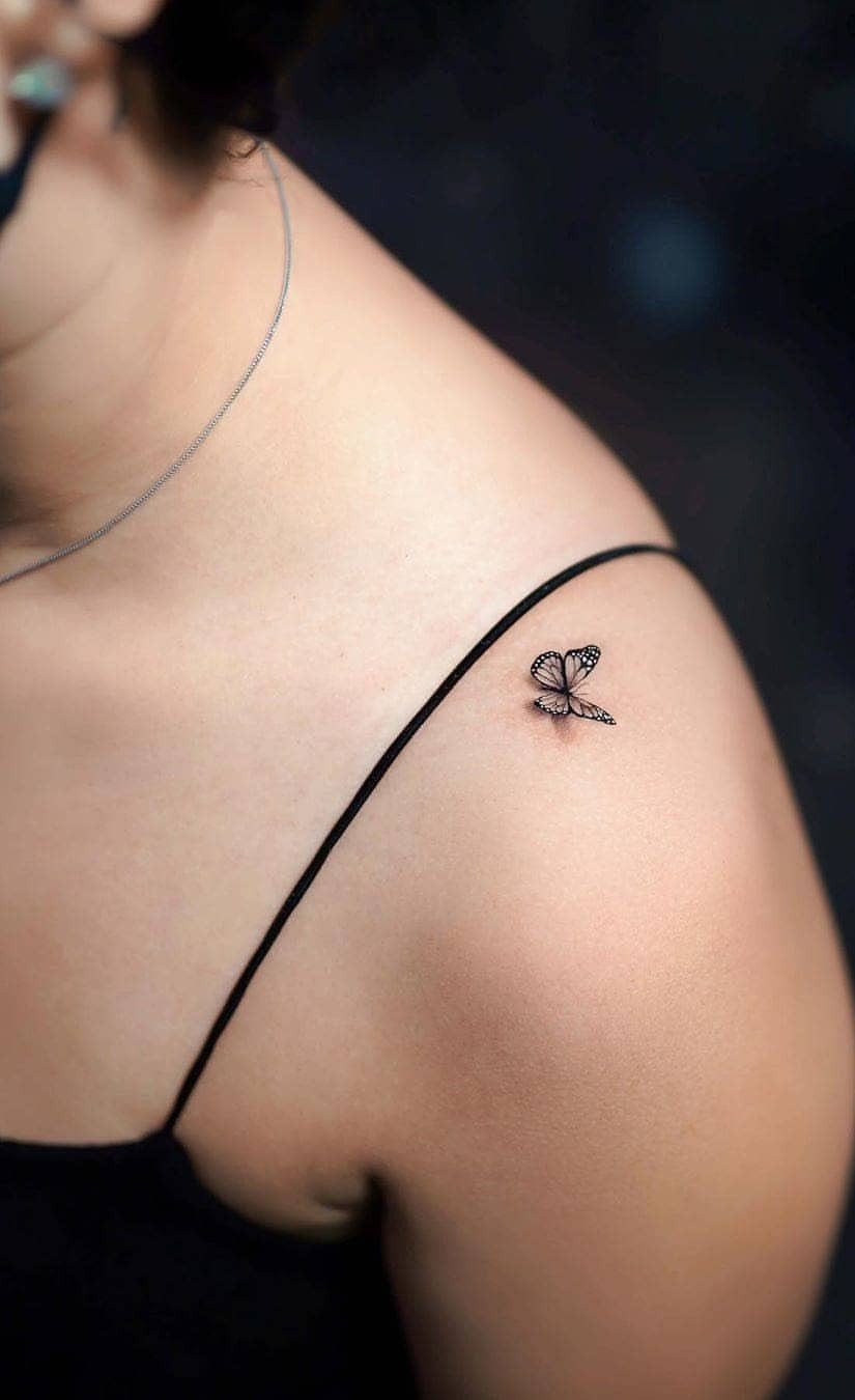 A small black ink butterfly tattoo positioned on a person's shoulder near the collarbone.