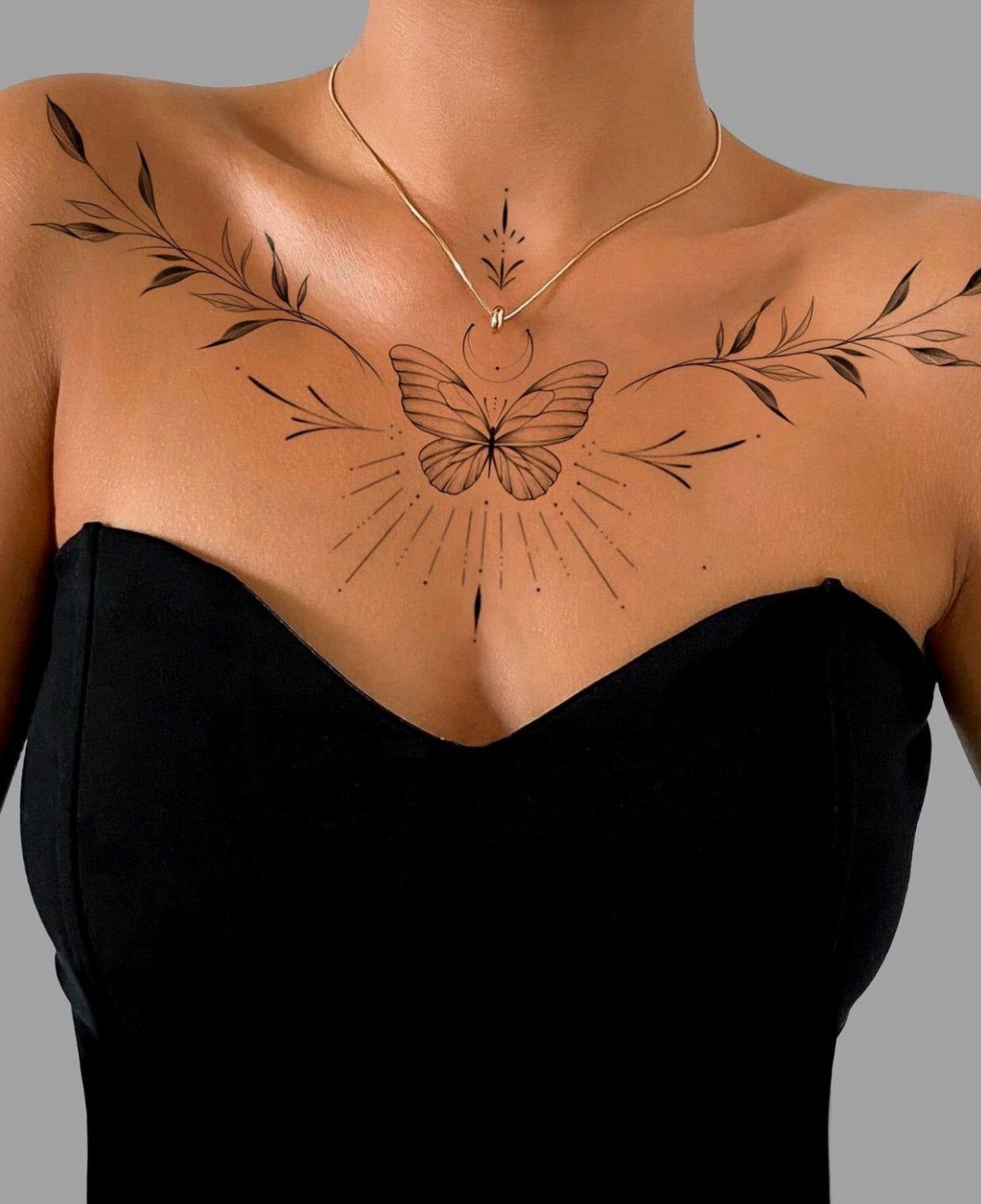Black ink butterfly tattoo with sunburst rays and leafy branches on a woman's collarbone.
