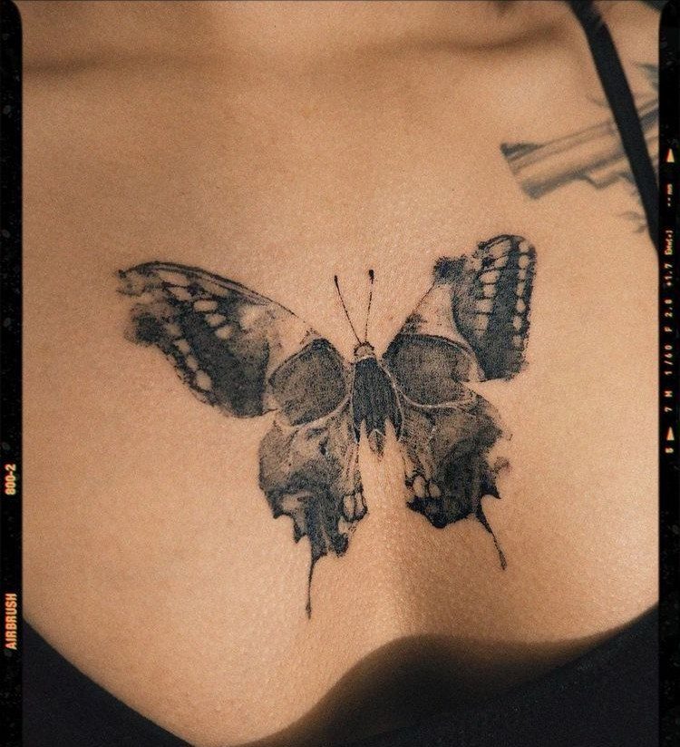 A large black ink butterfly tattoo positioned on a person's collarbone area.
