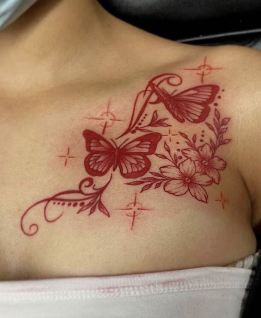 Red ink butterfly and floral tattoo on a person's collarbone with delicate swirling lines.