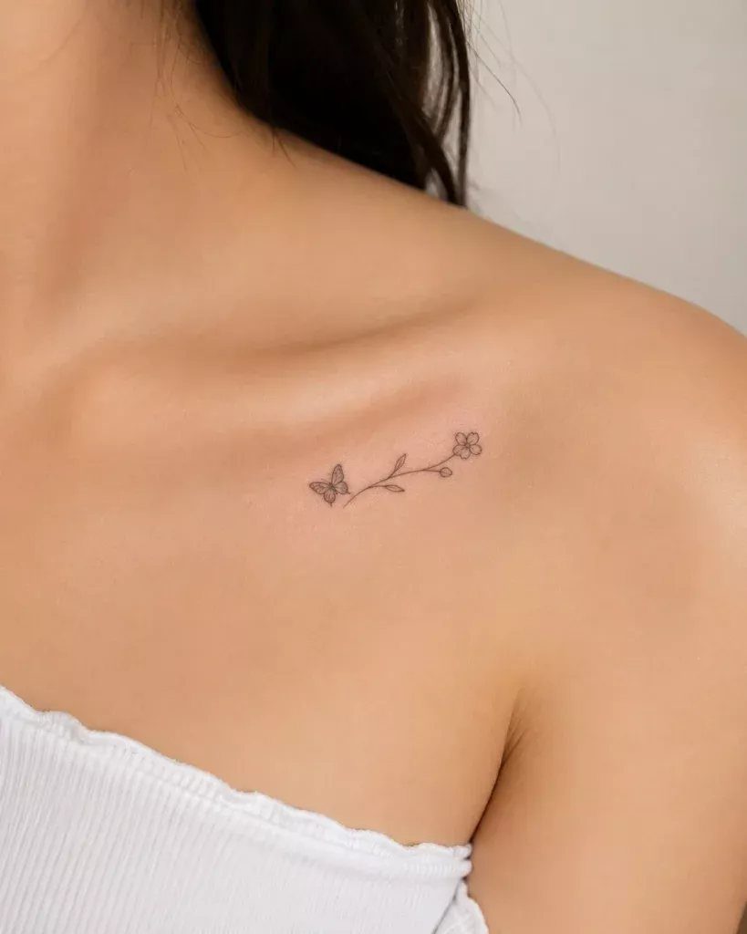 Small black ink butterfly and flower tattoo located on a person's collarbone.