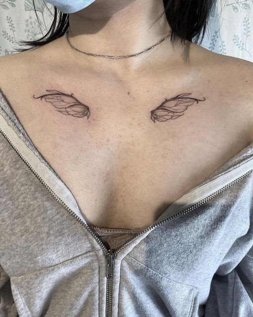 Two delicate black ink butterfly wing tattoos placed symmetrically on a person's collarbone.