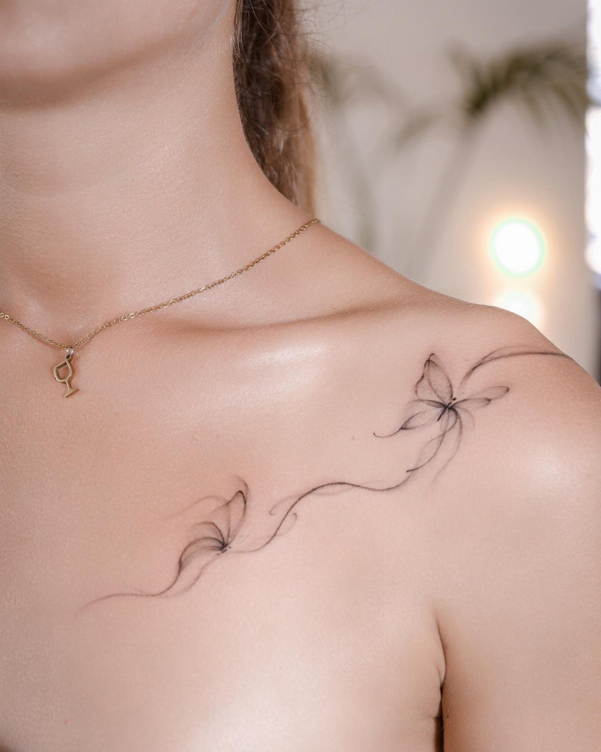 Two delicate black ink butterfly tattoos flowing along a woman's collarbone and shoulder.