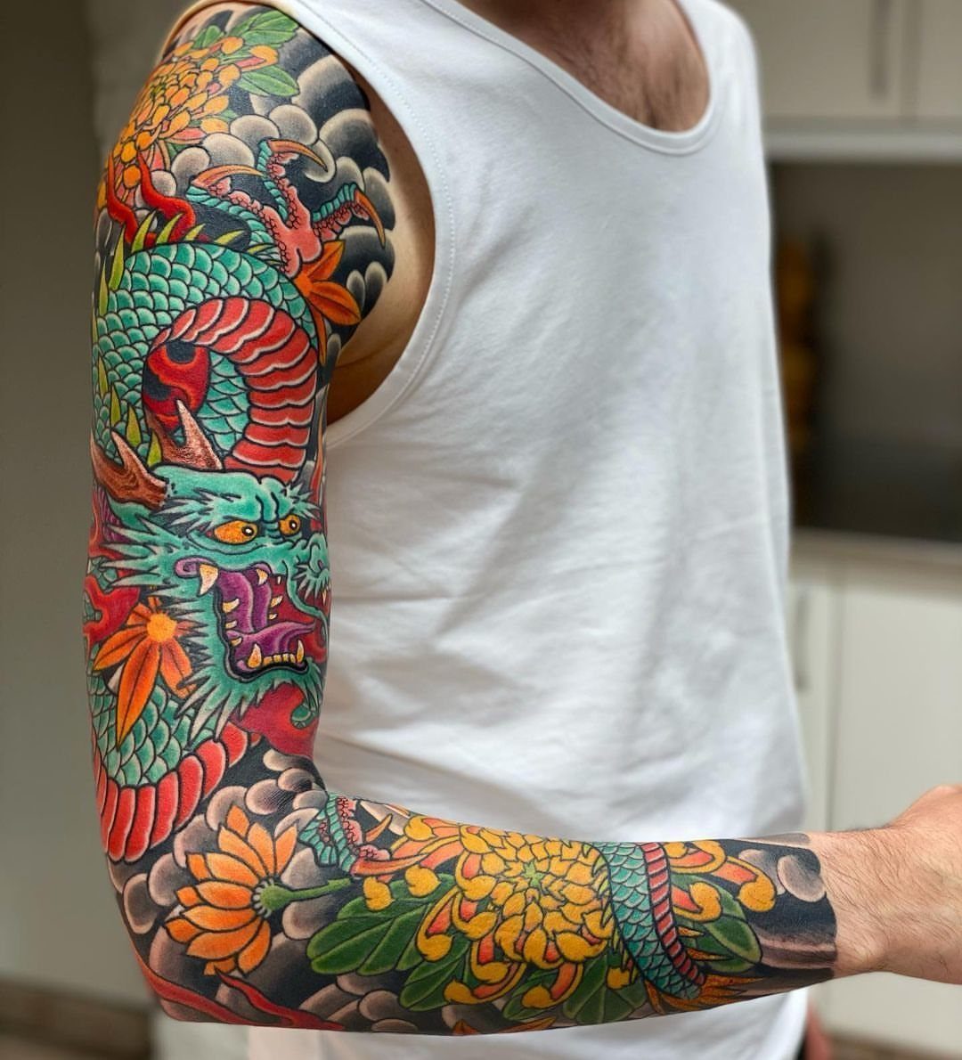 8 Color Tattoo Ideas for Men: Comic, Dragon & Watercolor 2 A man's arm displaying a large, colorful dragon sleeve tattoo with floral patterns.
