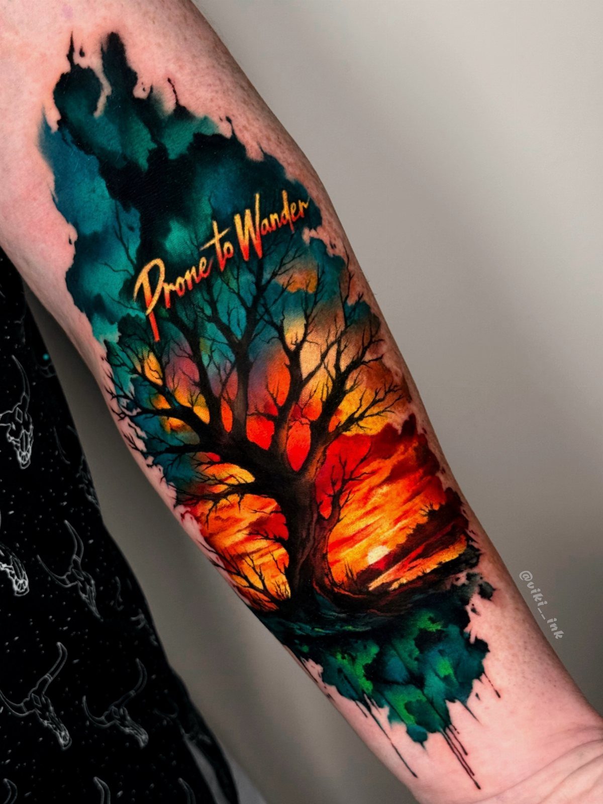 8 Color Tattoo Ideas for Men: Comic, Dragon & Watercolor 3 A watercolor style tattoo of a tree silhouette against a colorful sunset on a person's arm.