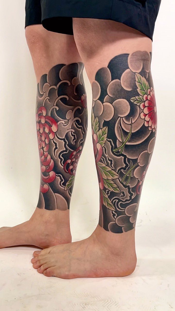 A person's legs displaying large, colorful Japanese-style tattoos with clouds and floral motifs.
