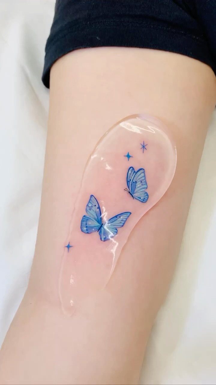 Two light blue butterfly tattoos with small stars on a person's arm.