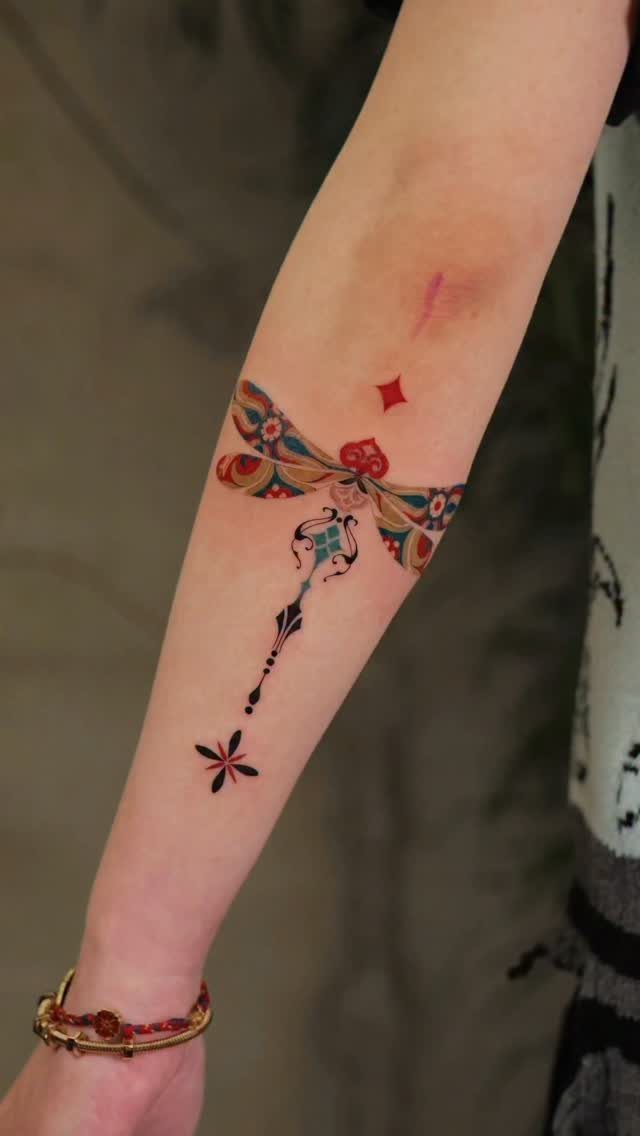A colorful, patterned dragonfly tattoo on a person's forearm with decorative star elements.