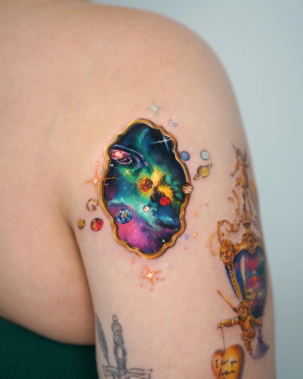 A colorful galaxy tattoo shaped like a gold frame on a person's shoulder.