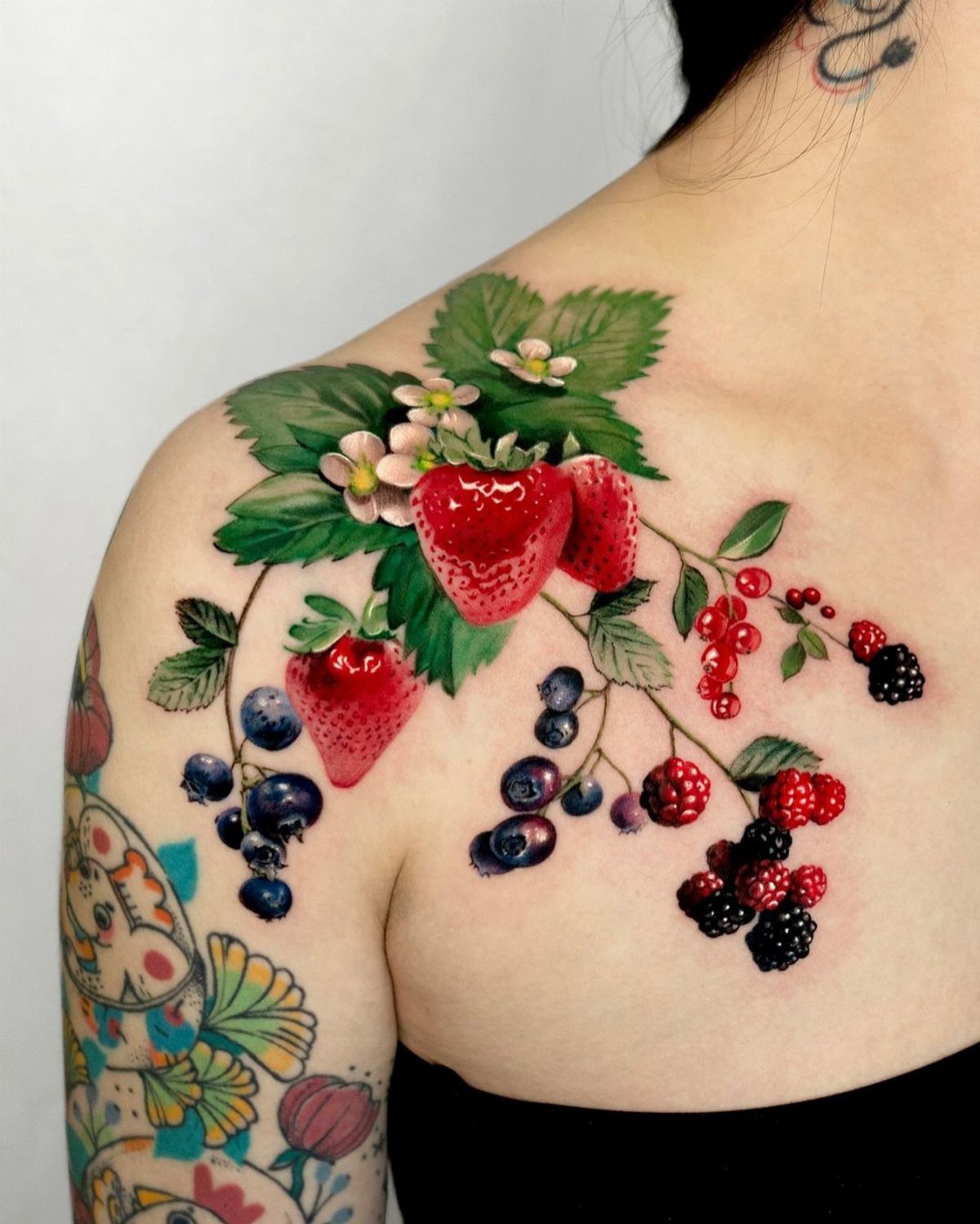A vibrant fruit tattoo featuring strawberries, berries, and green leaves on a person's shoulder.