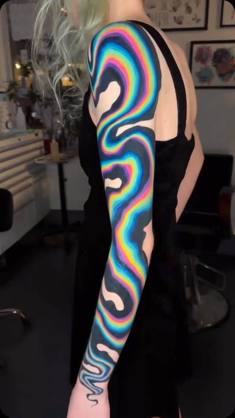 A person's arm featuring a large, vibrant neon psychedelic swirl sleeve tattoo.