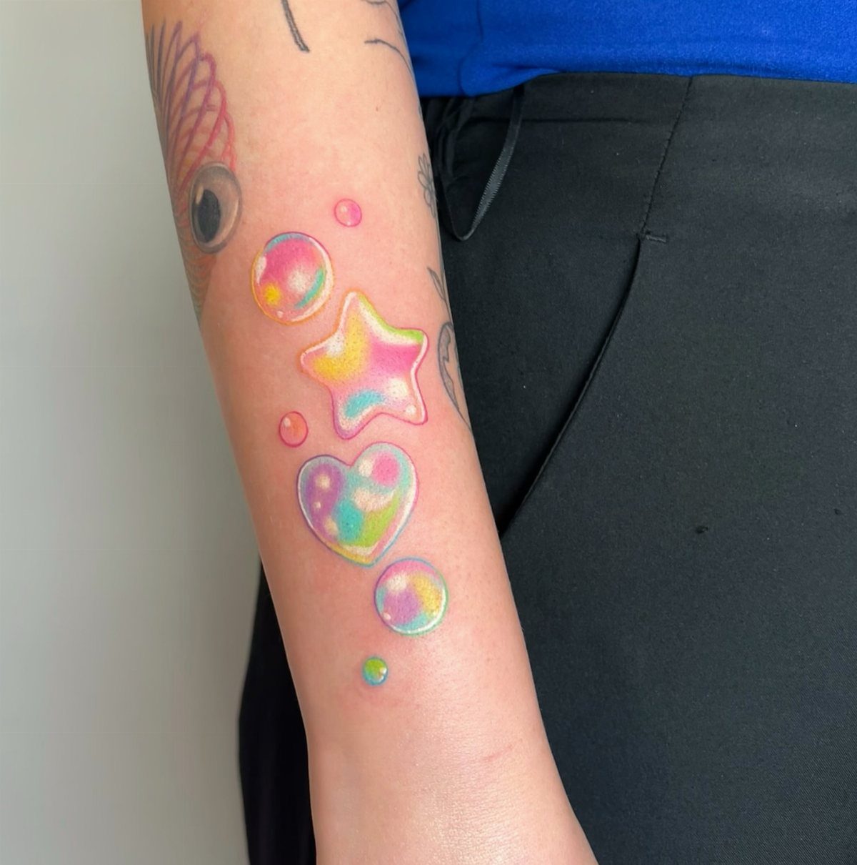 Pastel tattoos of a heart, star, and bubbles on a person's forearm.