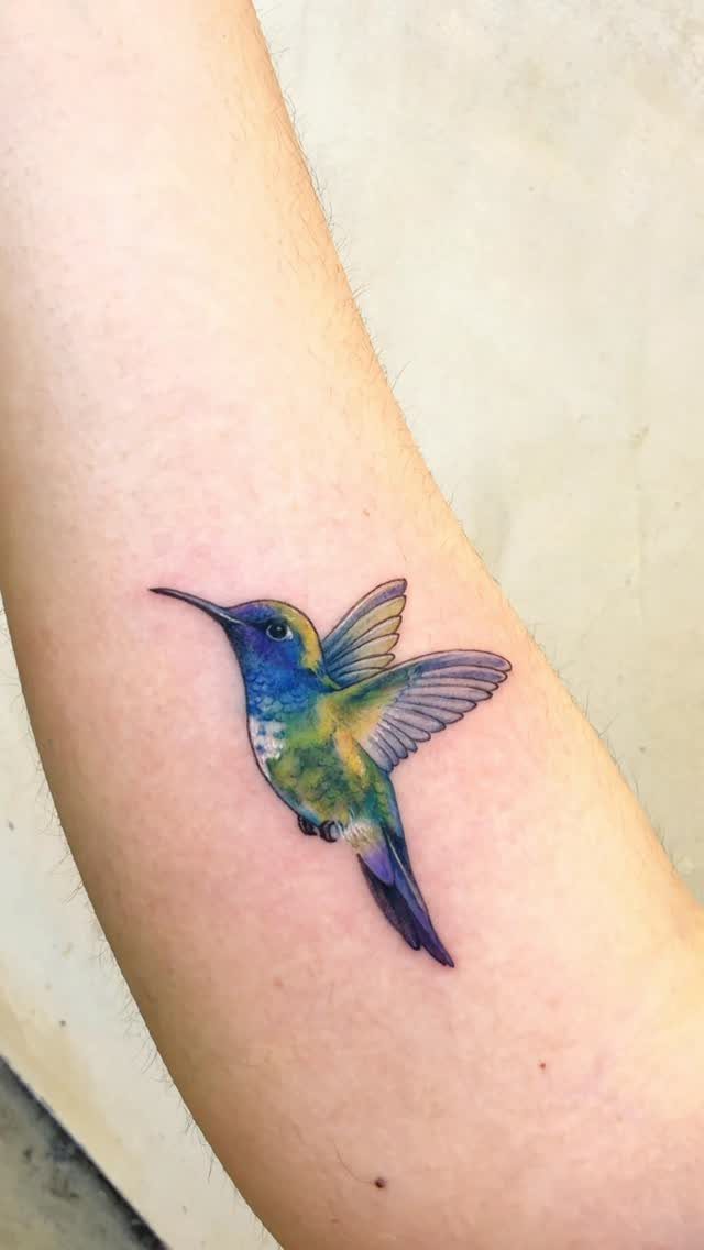 A colorful hummingbird tattoo with blue and yellow shading on a person's skin.