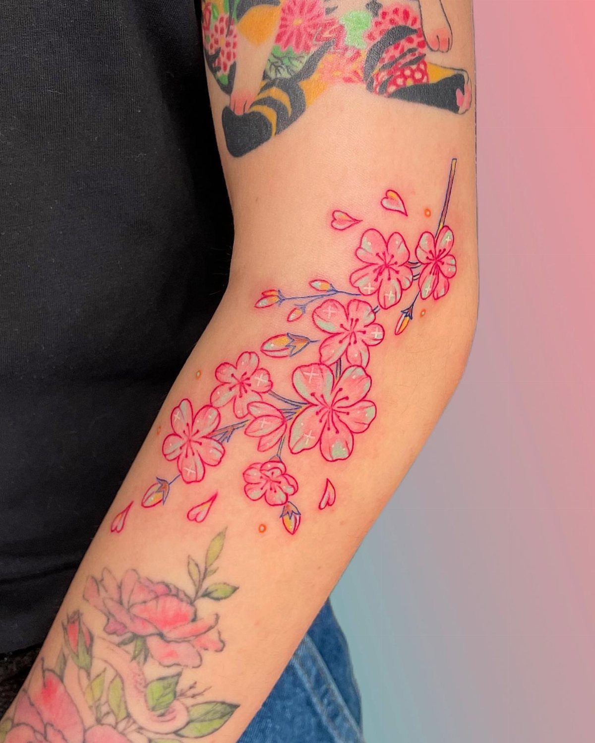 Pink cherry blossom branch tattoo with small hearts on a person's forearm.