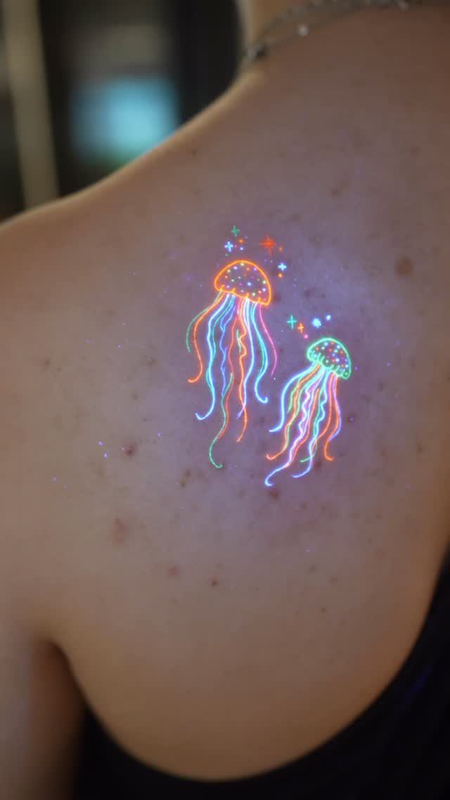 Two neon jellyfish tattoos with colorful stars on a person's shoulder.