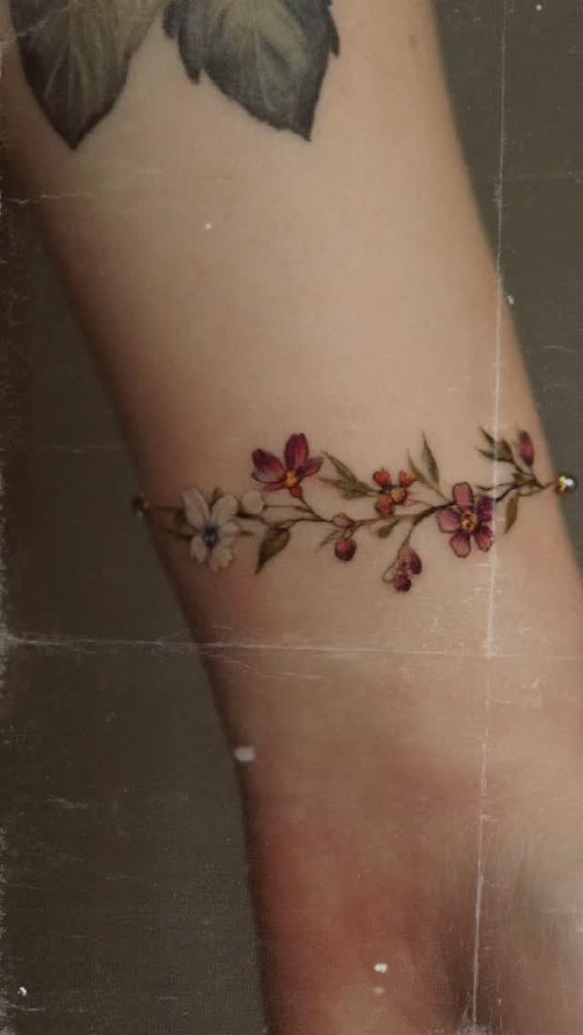 8 Dainty Timeless Tattoos for Minimal Ink That Lasts 8 A delicate floral vine tattoo with small colorful wildflowers wrapped around a person's wrist.