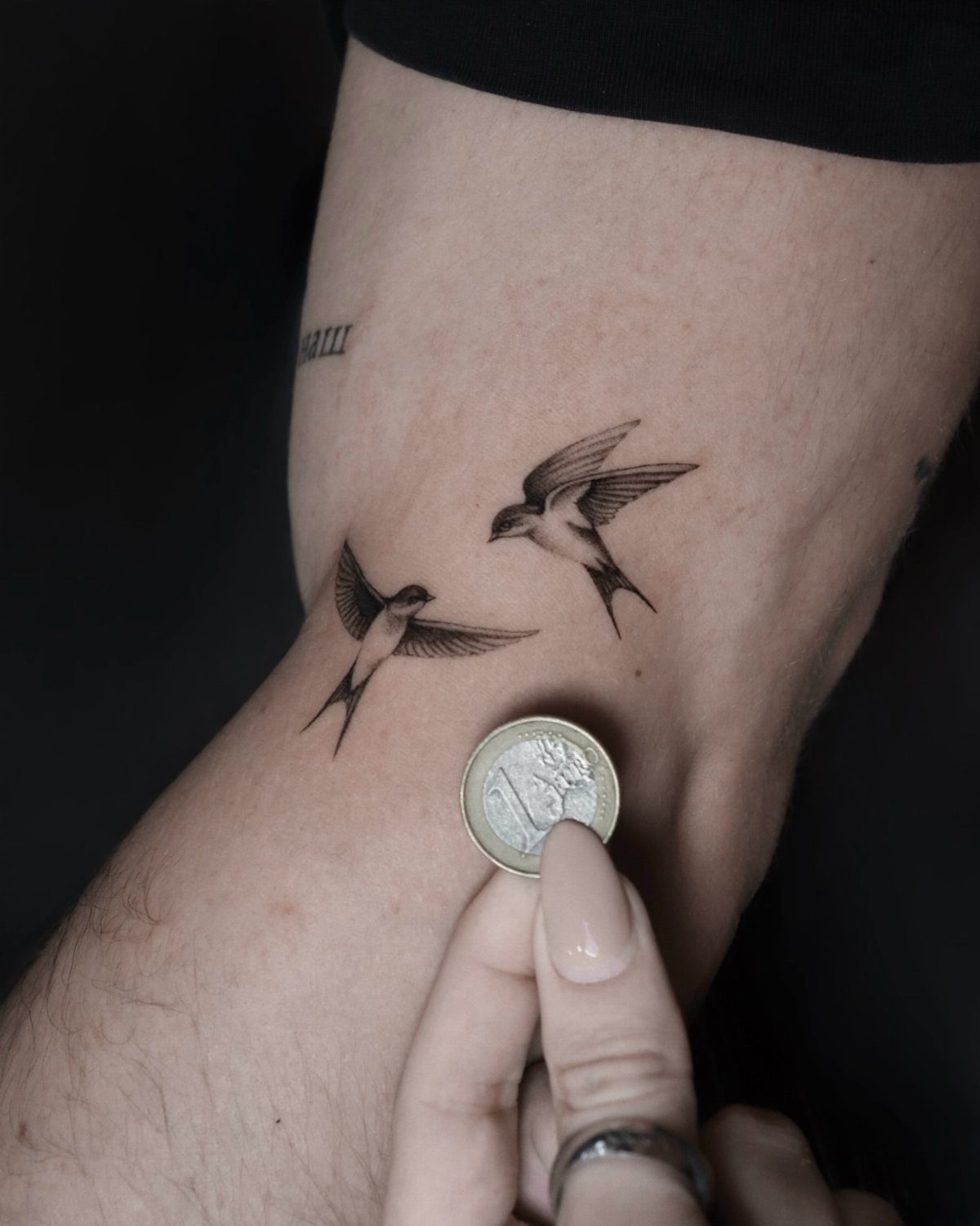 8 Dainty Timeless Tattoos for Minimal Ink That Lasts 2 Two small black ink swallow tattoos in flight on a person's leg next to a coin.