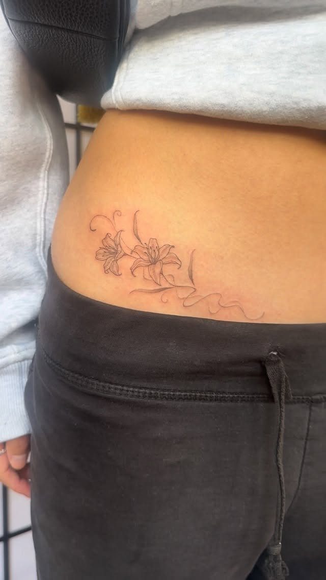 8 Dainty Timeless Tattoos for Minimal Ink That Lasts 6 A delicate fine line floral tattoo of two lilies on a person's hip.
