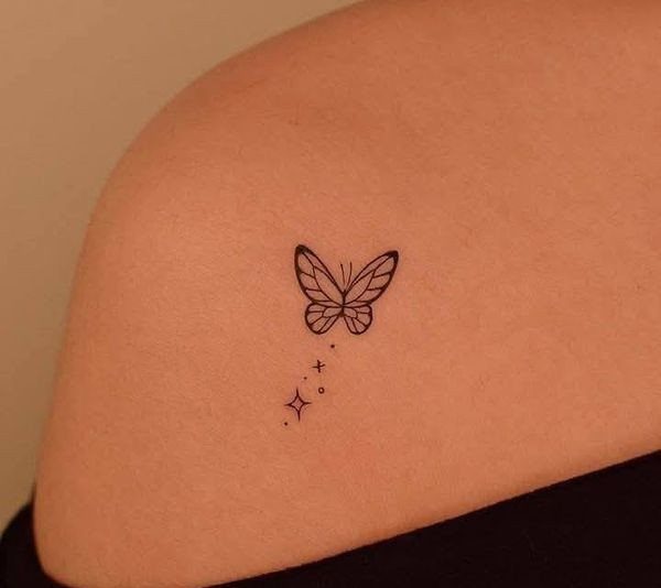 8 Dainty Timeless Tattoos for Minimal Ink That Lasts 1 A small black ink butterfly outline tattoo with tiny sparkles on skin.