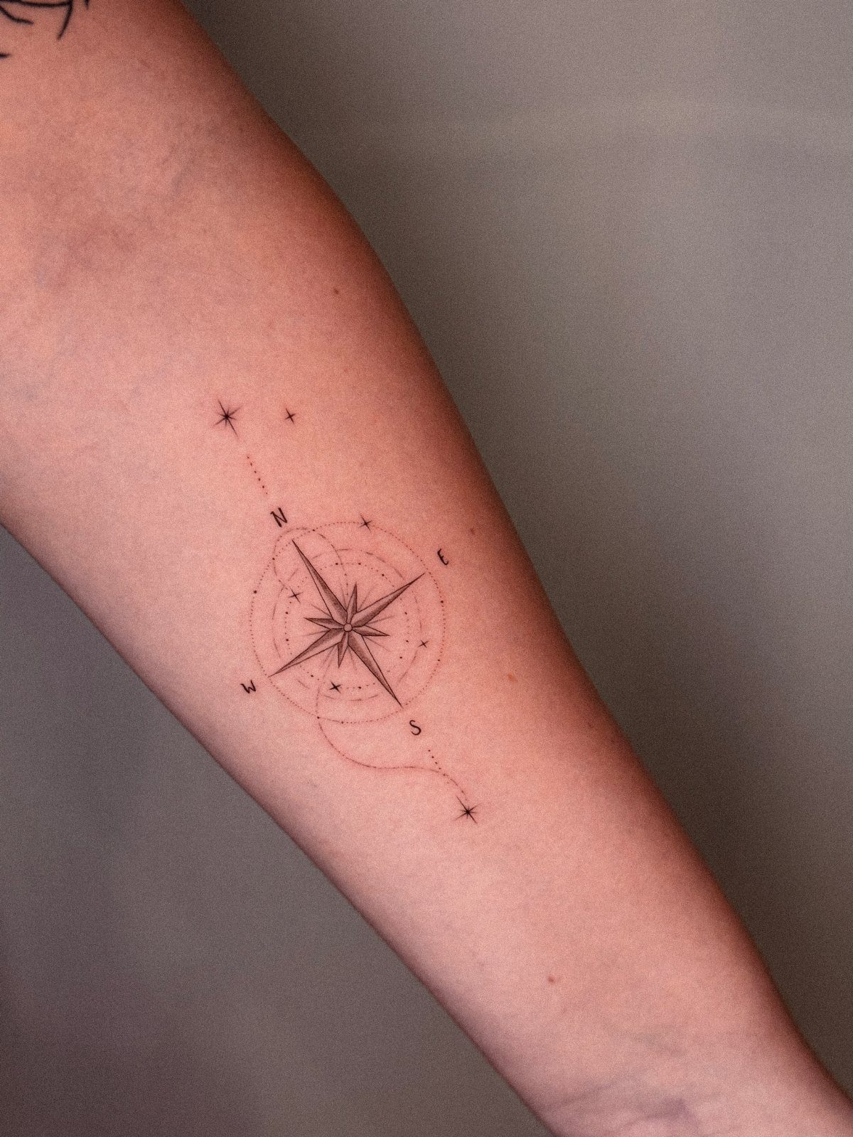 8 Dainty Timeless Tattoos for Minimal Ink That Lasts 4 A fine-line black ink compass rose tattoo with stars on a person's forearm.