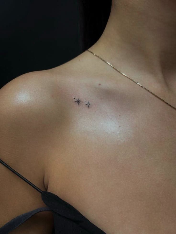 8 Dainty Timeless Tattoos for Minimal Ink That Lasts 3 Two tiny fine-line black ink four-pointed stars tattooed on a person's collarbone.