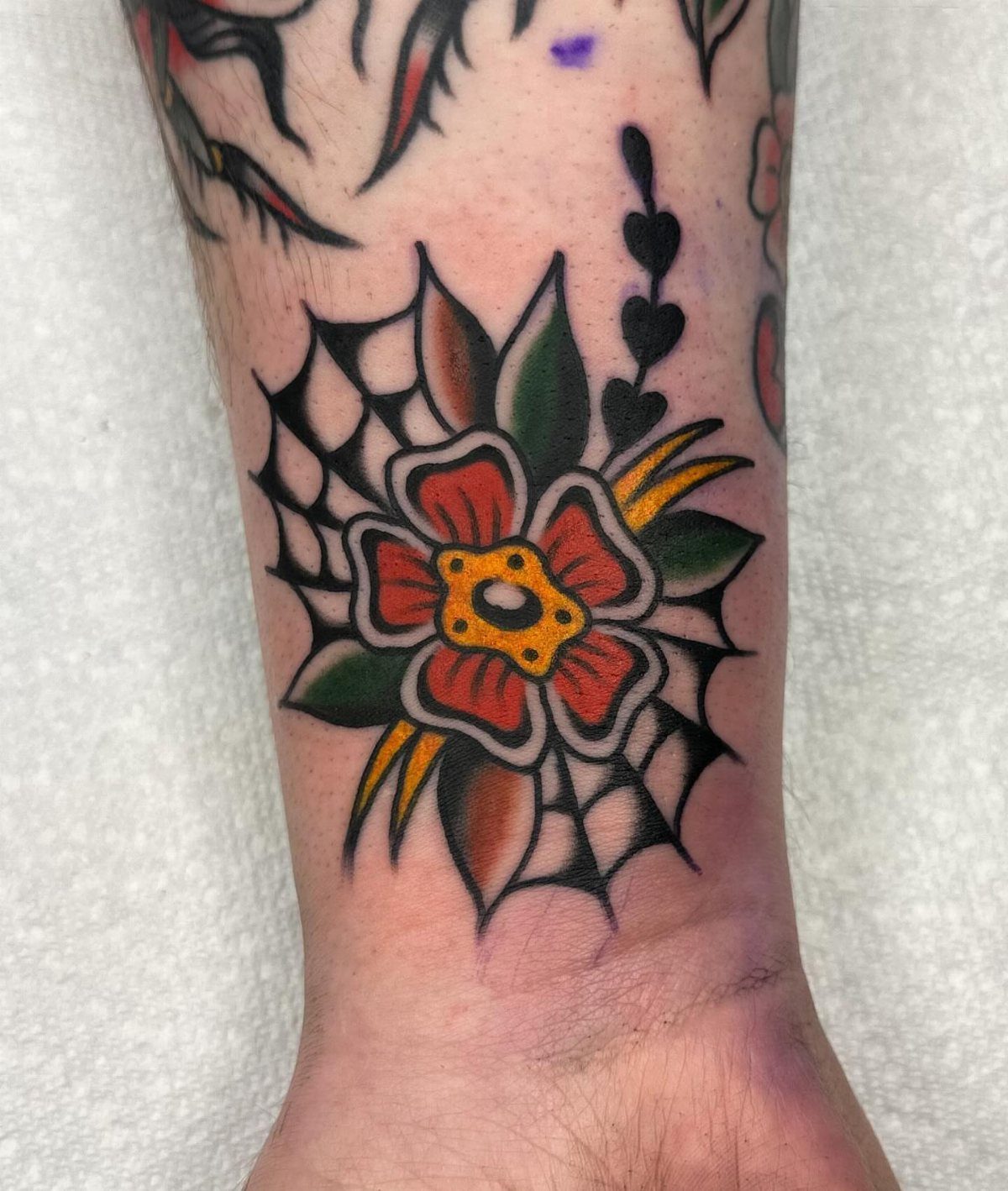 An American traditional style flower tattoo with red petals and green leaves on a person's arm.