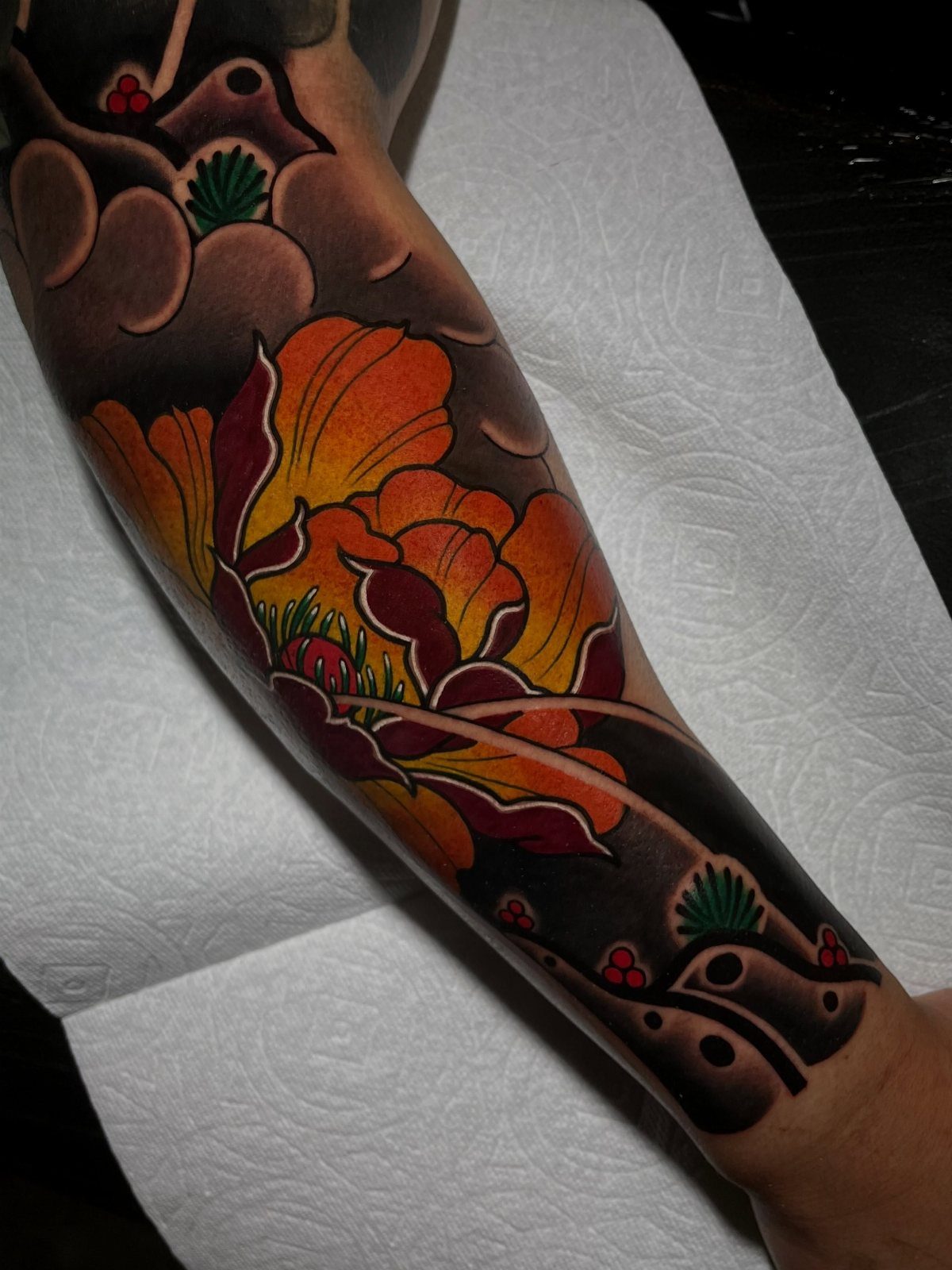 A colorful Japanese style sleeve tattoo featuring a large orange peony and dark grey clouds.