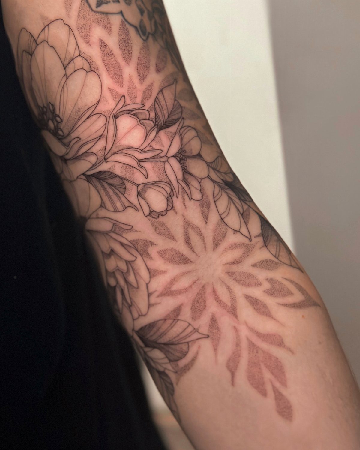 Detailed black ink tattoos of large flowers and mandala patterns on a person's arm.