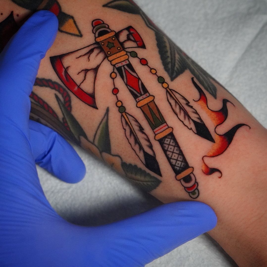 American traditional style tattoos of an axe with feathers and a flame on a person's arm.