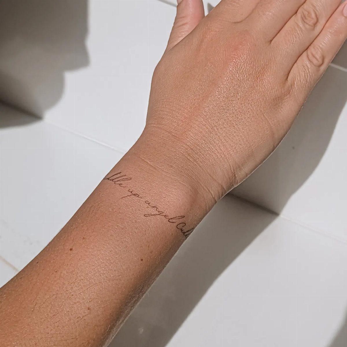 Fine Line Tattoo Aesthetic for Women: 9 Idea Boards 9 A person's wrist displaying a delicate fine line script tattoo in cursive lettering.