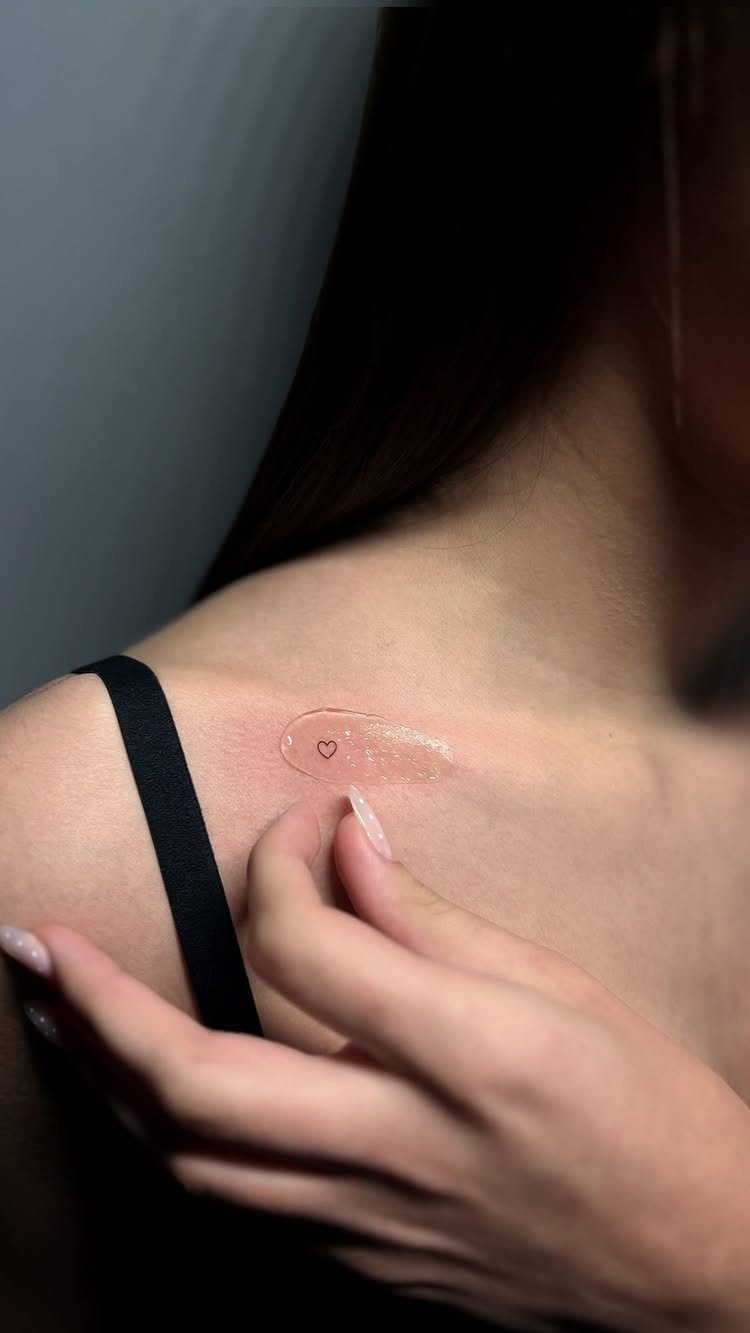 Fine Line Tattoo Aesthetic for Women: 9 Idea Boards 6 A small minimalist heart tattoo on a person's collarbone with a hand nearby.