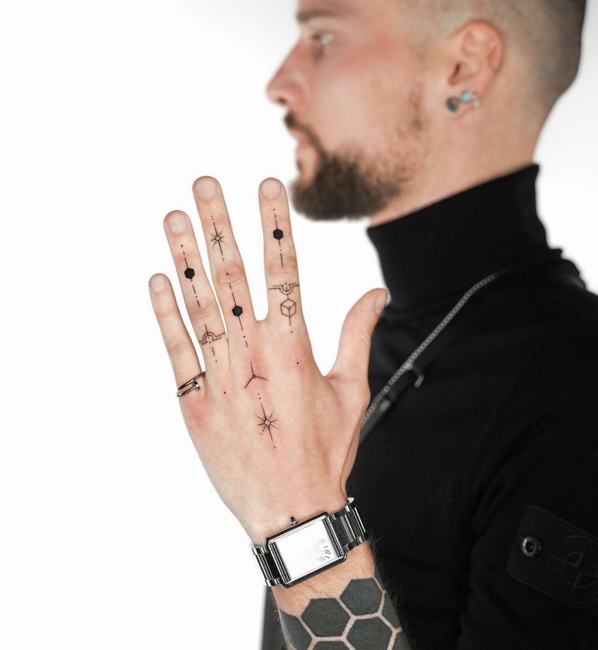 A man's hand displaying various small, black ink fine-line geometric tattoos on his fingers.