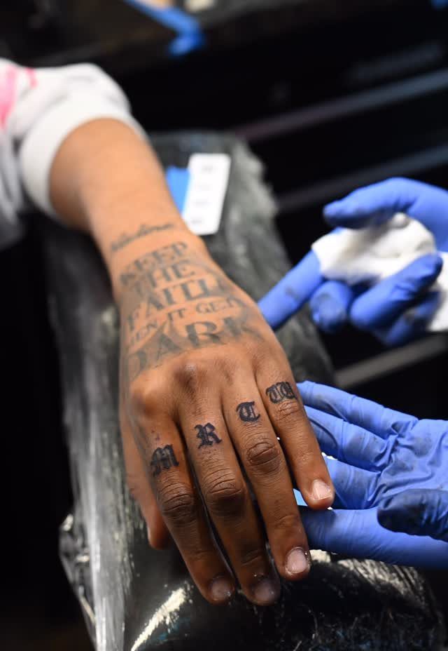 Hand with black Old English lettering tattoos on the knuckles and back of the hand.
